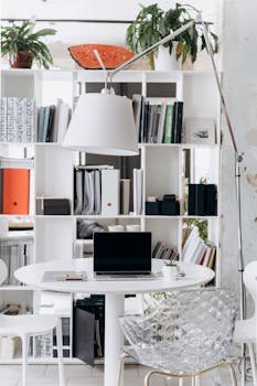 A stylish and minimalist home office setup featuring a laptop, books, and a modern lamp.